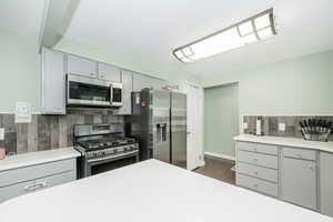 Kitchen featuring gray cabinets, tasteful backsplash, stainless steel appliances, and dark wood-style floors