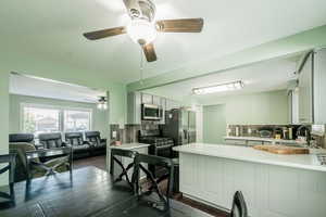 Kitchen with decorative backsplash, light countertops, stainless steel appliances, a peninsula, and dark wood-type flooring