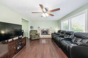 Living room with dark wood-style floors, a fireplace, and a ceiling fan