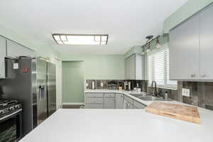 Kitchen featuring gray cabinetry, light countertops, stainless steel appliances, and decorative backsplash