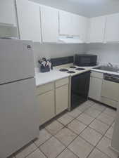 Kitchen featuring white appliances, light countertops, white cabinets, light tile patterned flooring, and range hood