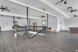 Living area featuring a textured ceiling, a ceiling fan, beamed ceiling, and dark wood-style flooring