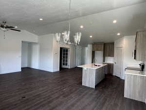 Kitchen featuring a center island with sink, open floor plan, dark wood finished floors, hanging light fixtures, and a chandelier