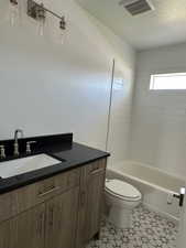 Bathroom with vanity, washtub / shower combination, light tile patterned floors, and a textured ceiling