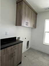 Laundry area with cabinet space, hookup for a washing machine, a textured ceiling, and electric dryer hookup