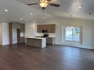 Kitchen featuring open floor plan, brown cabinets, a kitchen island with sink, appliances with stainless steel finishes, and dark wood-style flooring