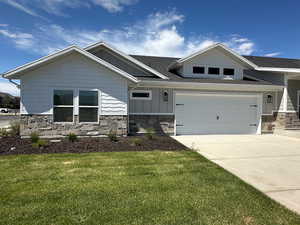 Craftsman-style house featuring stone siding, a shingled roof, driveway, a front yard, and board and batten siding