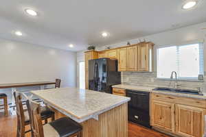 Kitchen with light countertops, decorative backsplash, dark wood finished floors, a kitchen island, and black appliances