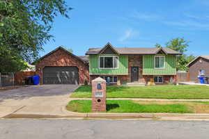 Raised ranch with board and batten siding, driveway, an attached garage, roof with shingles, and brick siding