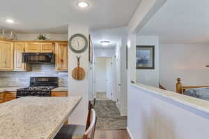 Kitchen featuring light countertops, tasteful backsplash, black appliances, dark wood-style flooring, and a breakfast bar area