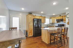 Kitchen featuring black appliances, a breakfast bar area, dark wood-type flooring, backsplash, and a center island