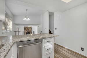 Kitchen featuring stainless steel dishwasher, white cabinets, light stone counters, and pendant lighting