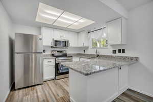 Kitchen featuring appliances with stainless steel finishes, a peninsula, light stone counters, and white cabinetry