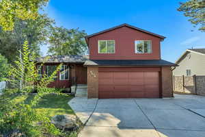Split level home with roof with shingles, a garage, driveway, and brick siding