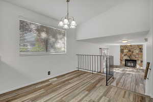 Unfurnished dining area with wood finished floors, a stone fireplace, and a chandelier