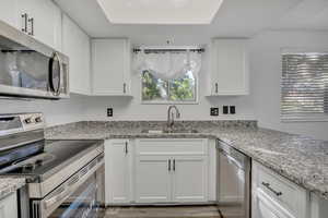 Kitchen with stainless steel appliances, white cabinetry, light stone countertops, and light wood-style floors