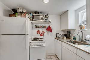 Unit C kitchen featuring white appliances, white cabinets, tasteful backsplash, light tile patterned floors, and light countertops.