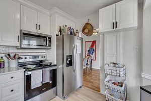Unit A kitchen featuring stainless steel appliances, white cabinets, decorative backsplash, and light wood-style floors.