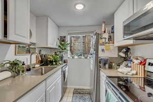 Unit B kitchen with appliances with stainless steel finishes, white cabinetry, light tile patterned flooring, and light  counters.