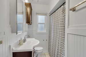 Unit A full bathroom featuring a wainscoted wall, vanity, light tile patterned floors, and a shower with curtain.