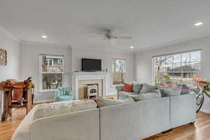 Unit A living area with light wood-style flooring, ornamental molding, plenty of natural light, a ceiling fan, and recessed lighting.