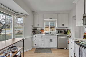 Unit A kitchen featuring backsplash, stainless steel appliances, white cabinetry, and light wood-type flooring.