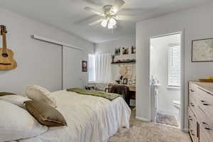 Unit A bedroom with ensuite half bath inside.. with light carpet, a closet, and a ceiling fan.