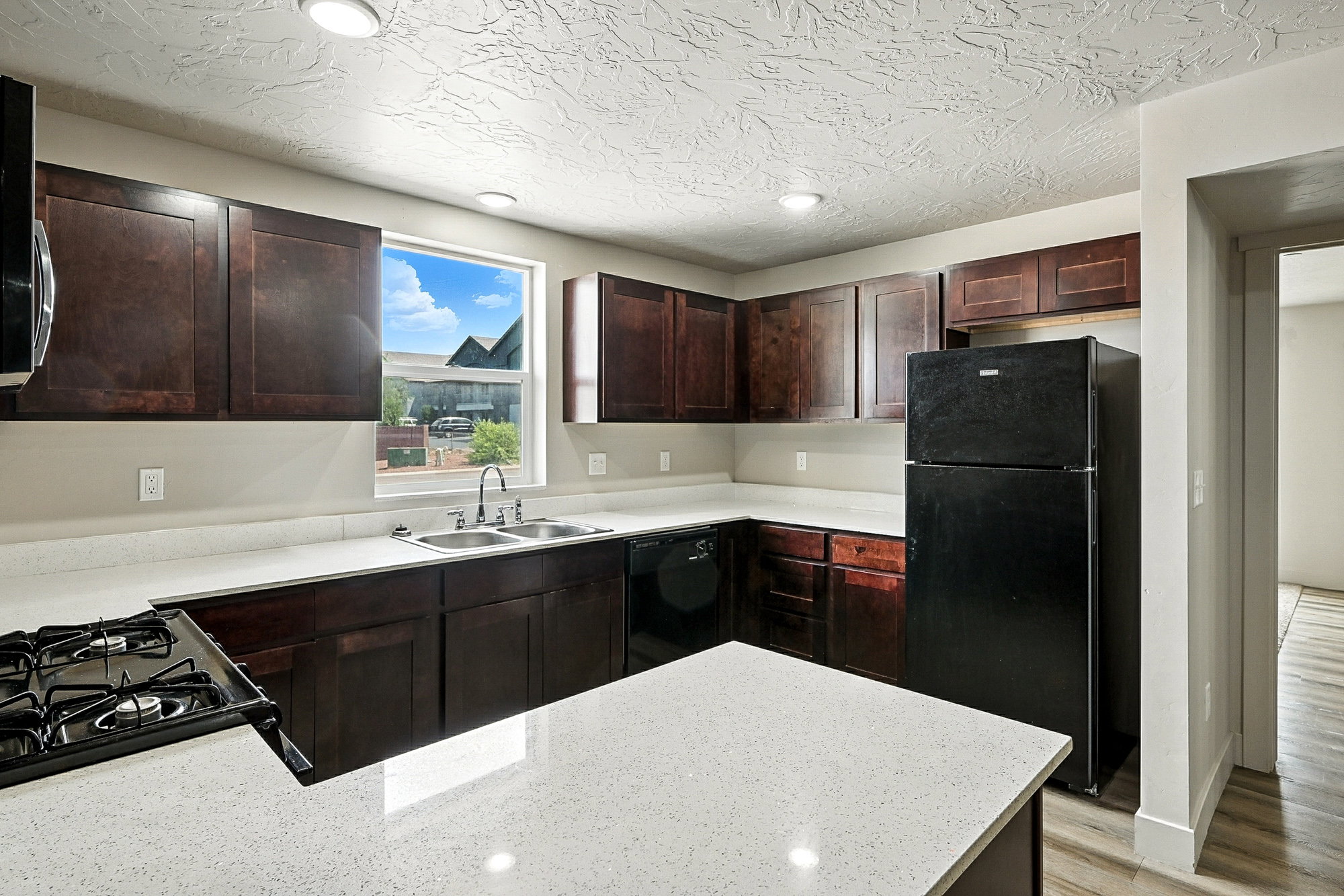 Kitchen with black appliances, dark brown cabinetry, a peninsula, light wood-style flooring, and light stone counters