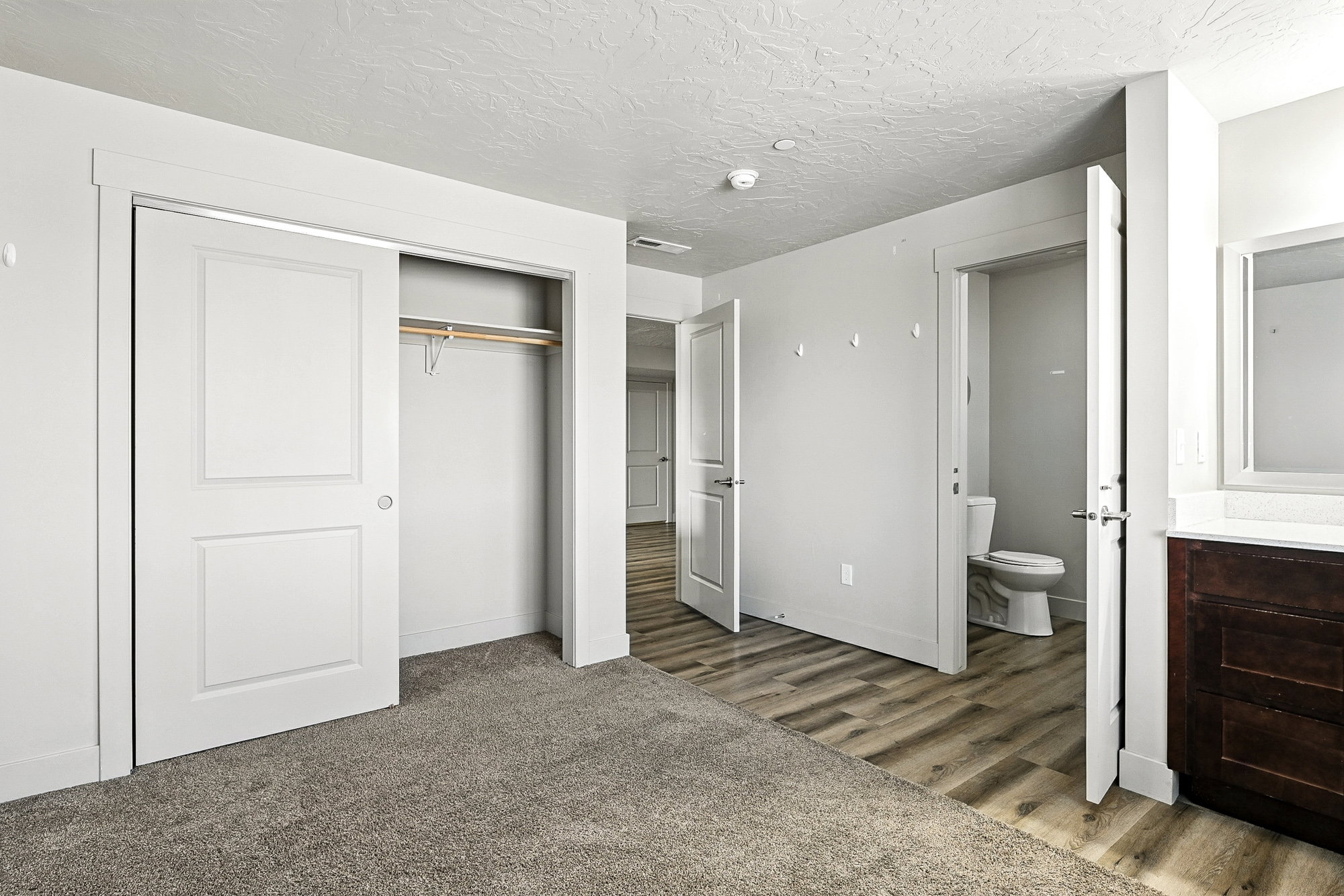 Unfurnished bedroom featuring a closet, a textured ceiling, light wood-style floors, ensuite bathroom, and light colored carpet