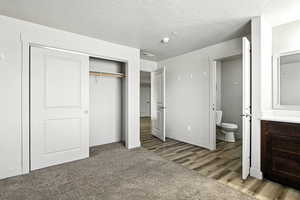 Unfurnished bedroom featuring a closet, a textured ceiling, light wood-style floors, ensuite bathroom, and light colored carpet
