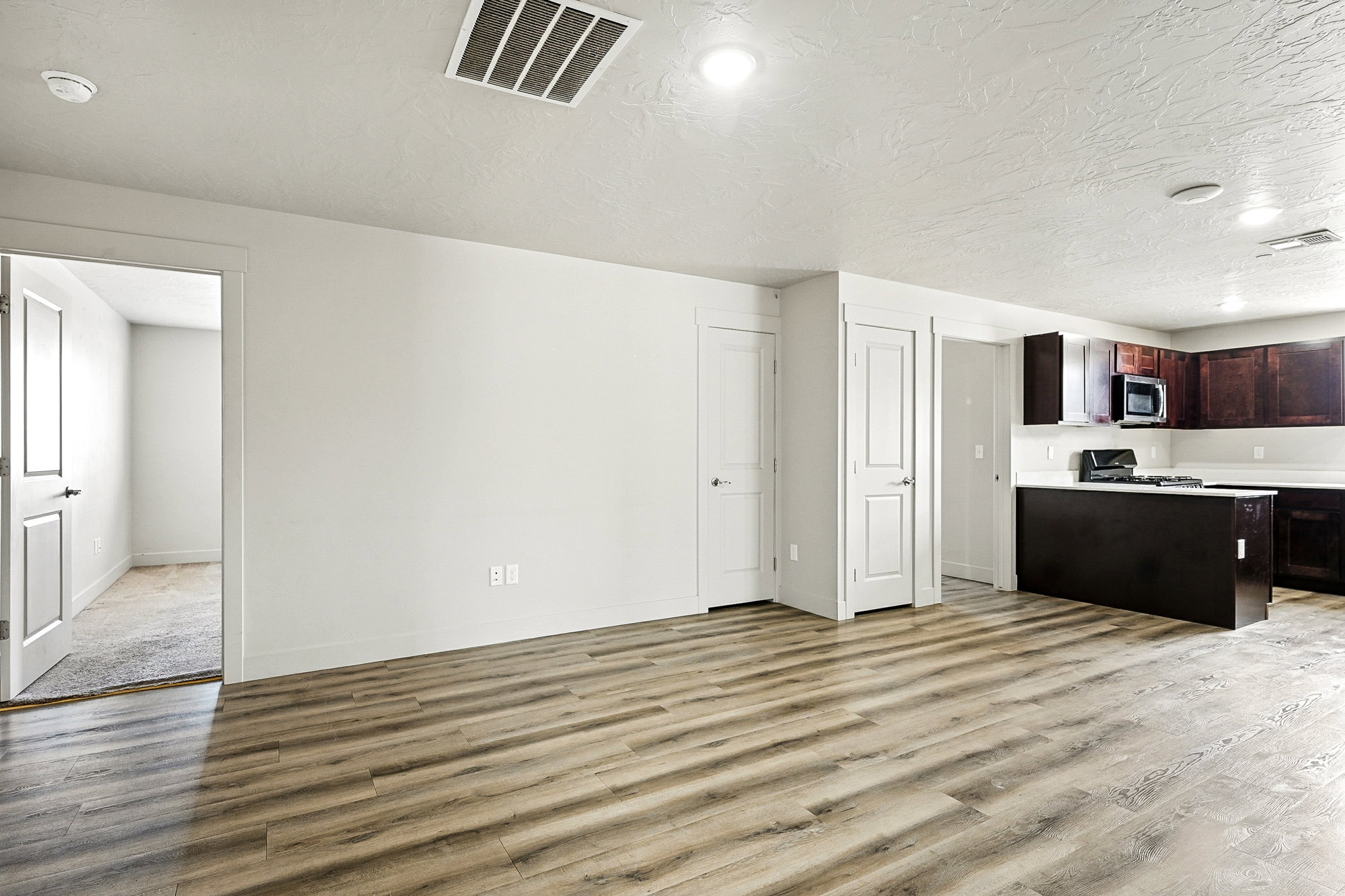 Kitchen featuring light countertops, light wood-style floors, dark brown cabinetry, a textured ceiling, and stainless steel microwave
