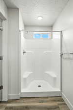 Full bathroom featuring a shower stall, wood finished floors, and a textured ceiling