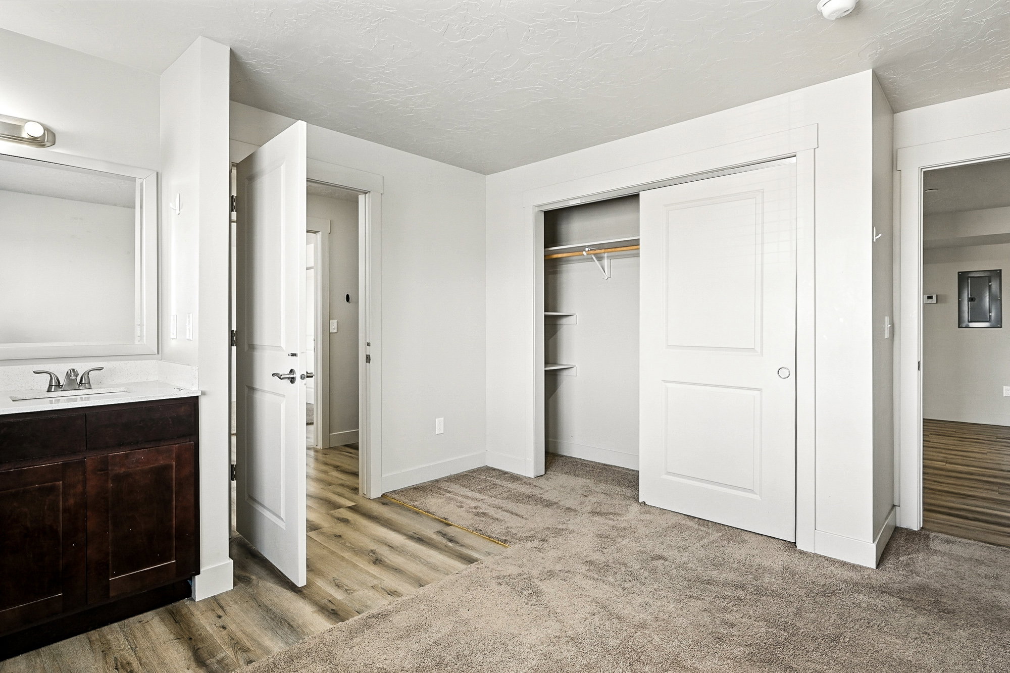 Unfurnished bedroom featuring a textured ceiling, a closet, light carpet, electric panel, and light wood finished floors
