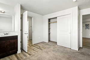 Unfurnished bedroom featuring a textured ceiling, a closet, light carpet, electric panel, and light wood finished floors