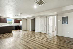 Unfurnished living room featuring electric panel, a textured ceiling, and light wood-type flooring