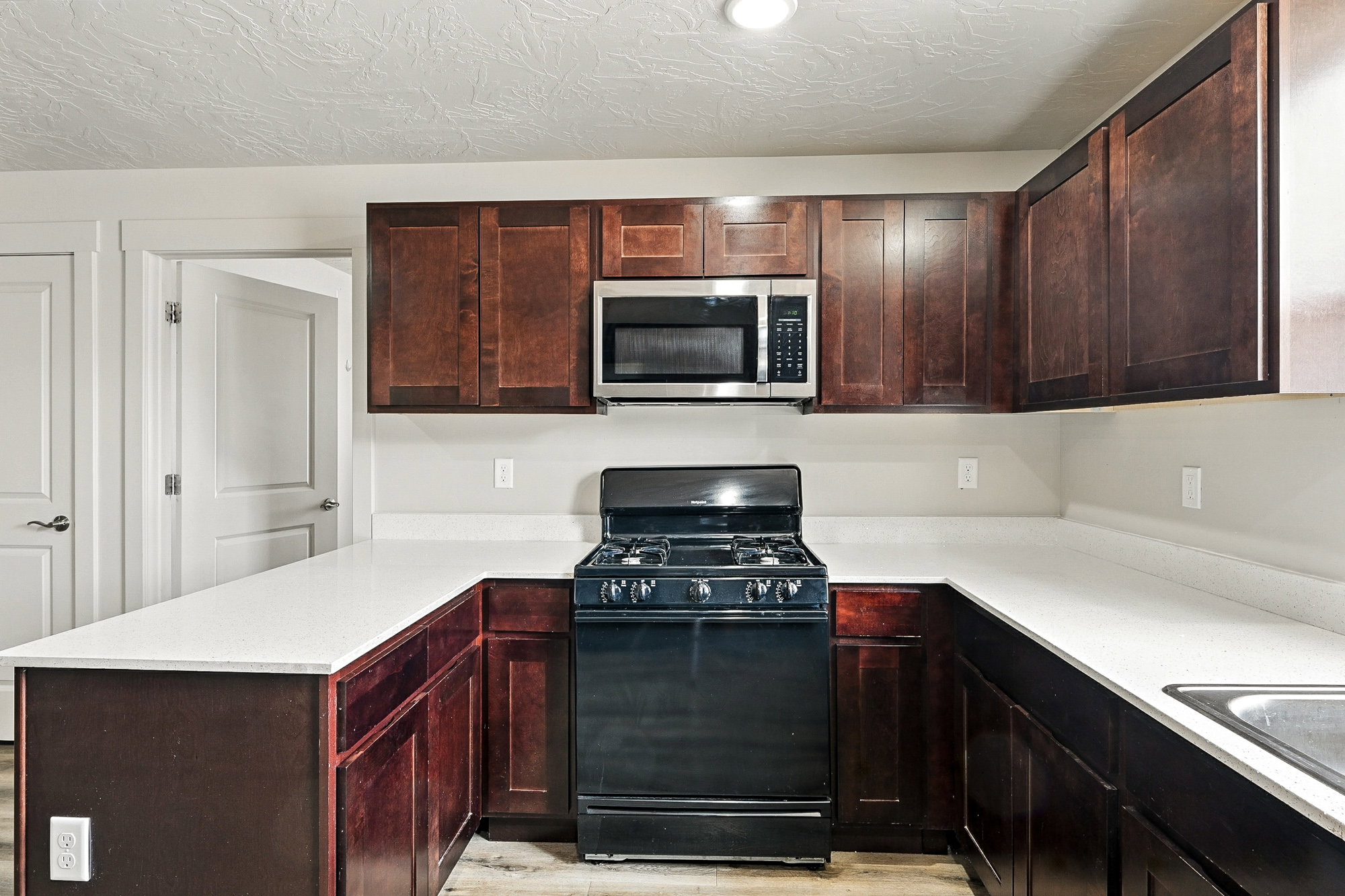 Kitchen with black gas stove, stainless steel microwave, a peninsula, a textured ceiling, and light wood-style flooring