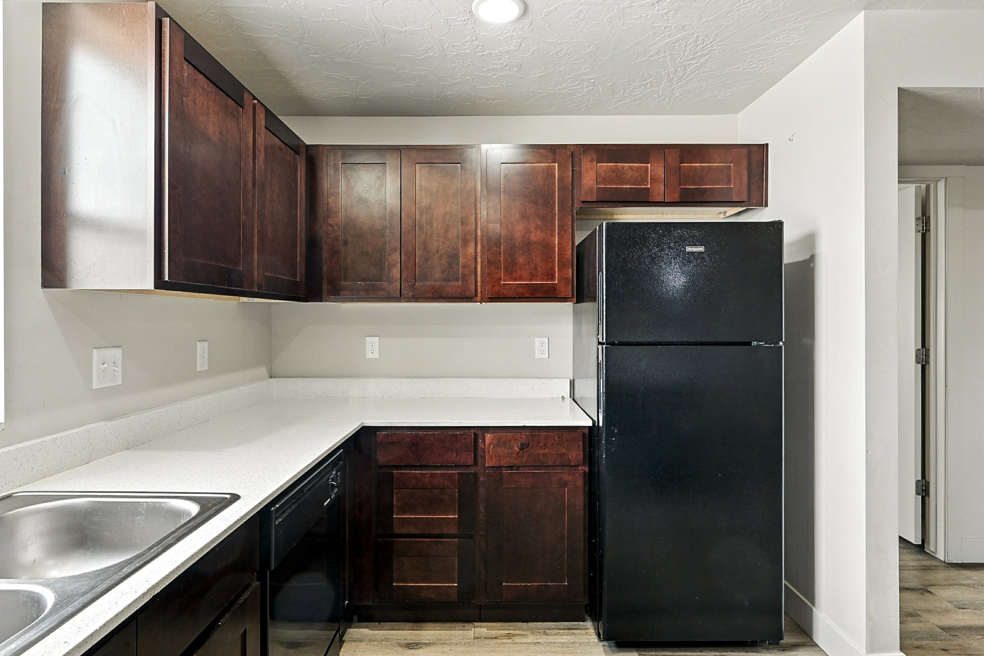 Kitchen with black appliances, light countertops, light wood finished floors, a textured ceiling, and dark brown cabinetry