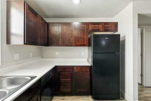 Kitchen with black appliances, light countertops, light wood finished floors, a textured ceiling, and dark brown cabinetry