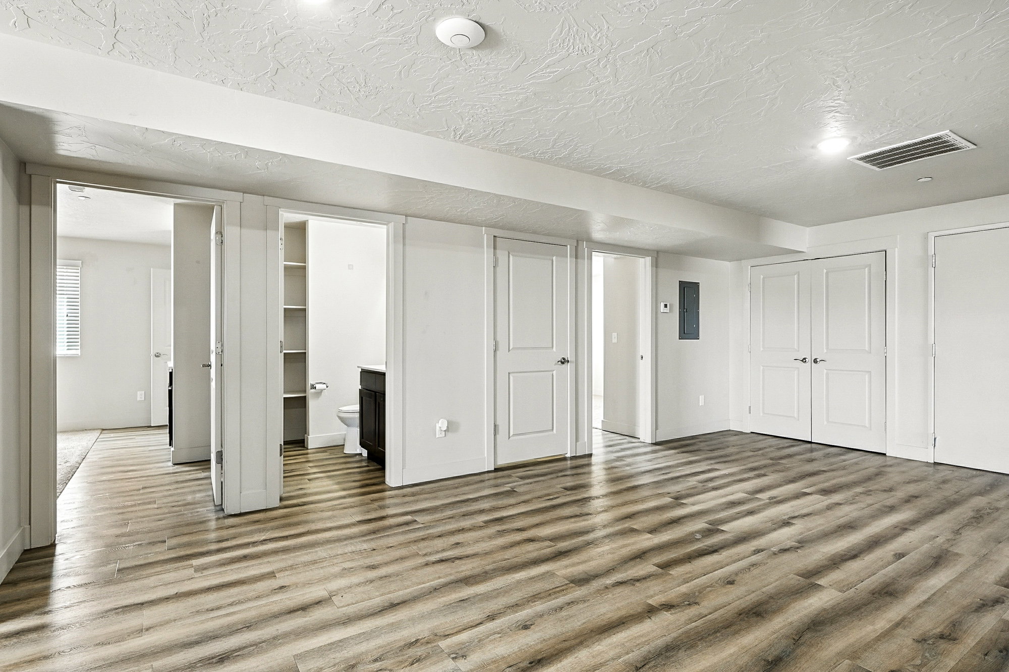 Unfurnished bedroom featuring wood finished floors, connected bathroom, a textured ceiling, electric panel, and multiple closets