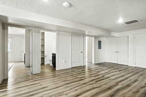 Unfurnished bedroom featuring wood finished floors, connected bathroom, a textured ceiling, electric panel, and multiple closets