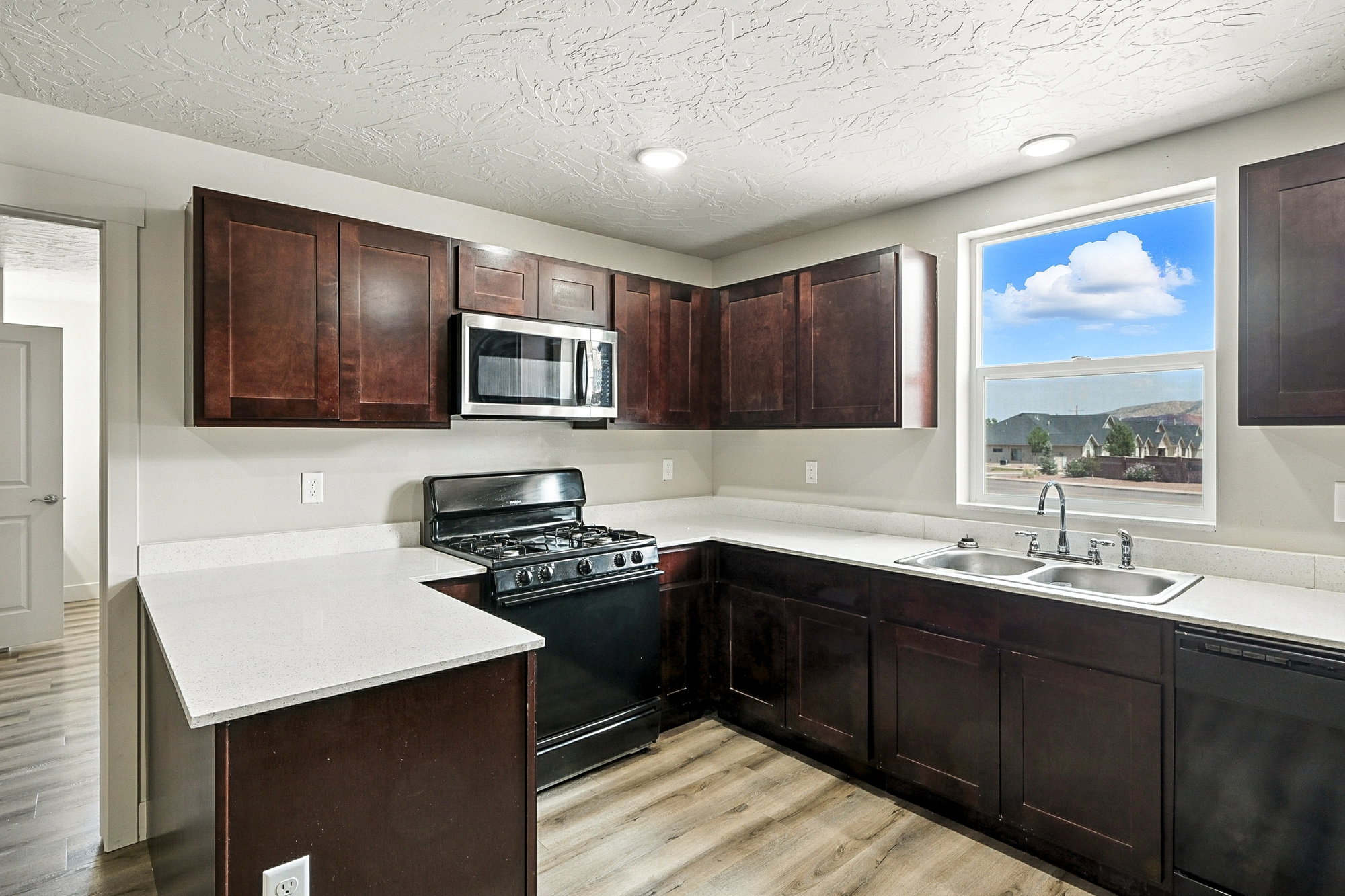 Kitchen with black appliances, dark brown cabinets, light wood-type flooring, a peninsula, and a textured ceiling