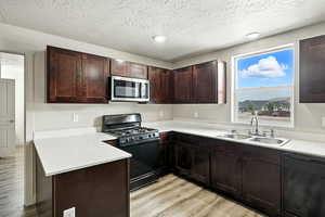 Kitchen with black appliances, dark brown cabinets, light wood-type flooring, a peninsula, and a textured ceiling