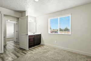 Unfurnished bedroom with a textured ceiling, light carpet, and ensuite bath