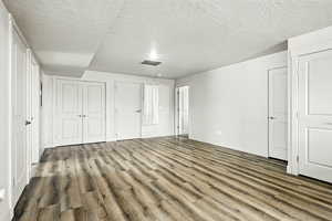 Unfurnished bedroom with wood finished floors, two closets, and a textured ceiling