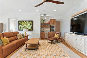 Living room with light wood-type flooring, wallpapered walls, a ceiling fan, beverage cooler, and recessed lighting