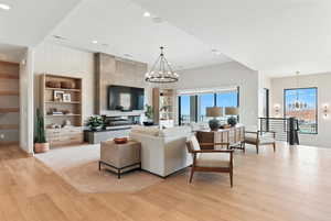 Living room with a chandelier, a tile fireplace, light wood finished floors, recessed lighting, and built in features