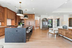 Kitchen with a kitchen bar, a large island, brown cabinets, decorative light fixtures, and recessed lighting