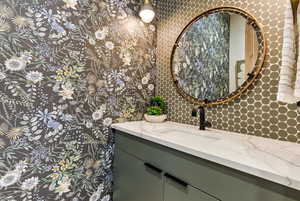 Bathroom with decorative backsplash, vanity, and wallpapered walls