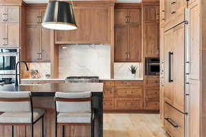 Kitchen featuring tasteful backsplash, appliances with stainless steel finishes, brown cabinetry, and light wood-style flooring