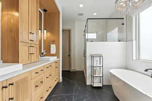 Bathroom featuring a stall shower, a freestanding tub, dark marble finish floors, double vanity, and recessed lighting